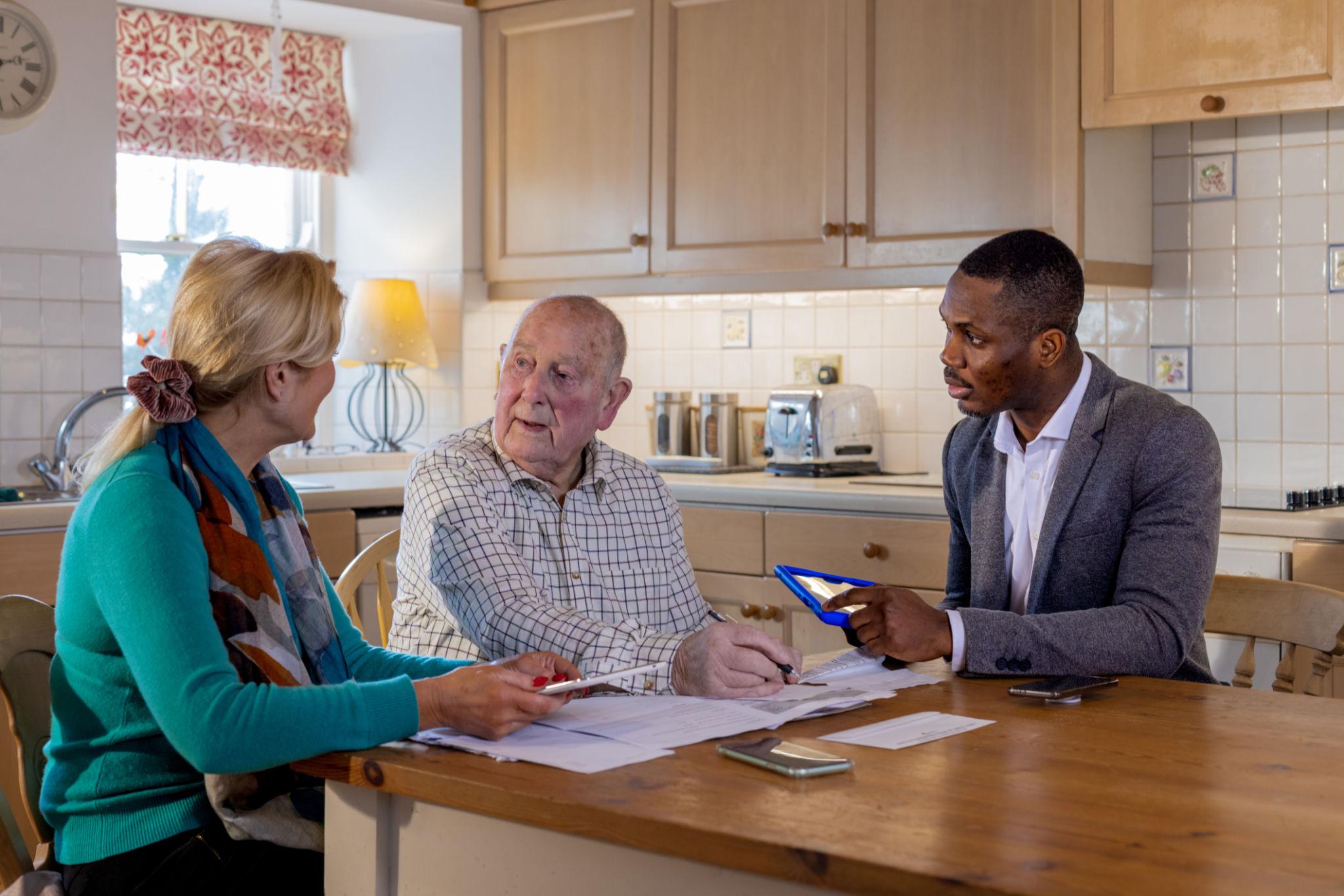 An older adult and two advisers discussing care and household documents together.